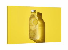 Detox beverage with lemon slices in a transparent bottle casting strong shadows in bright light on a yellow surface. Health, nutrition, and clean eating theme. Contemporary glass water container