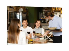 In restaurant, man waiter serves couple customer order, put plate with colorful salad of vegetables and cheese in front of guest. Cozy cafe establishment for family lunch, business meeting, coffee