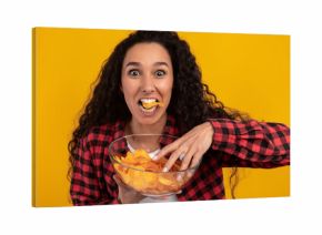 A joyful Latin woman is having a great time eating potato crisps.