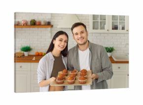 Happy young couple holding tray with yummy self baked tasty muffins out of oven, enjoy cooking in modern kitchen, homemade family pastries, culinary hobby, cupcakes dessert, tasty hot fresh bakery