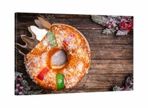 Roscon de reyes with cream and christmas ornaments on a wooden background, top view. Roscon is a traditional Spanish Christmas pastry cake with decoration. Kings day concept spanish three kings cake.