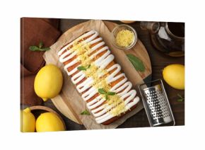 Tasty lemon cake decorated with icing, zest and mint served on wooden table, flat lay