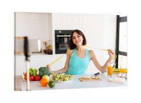 A young woman smiles while holding a measuring tape in a vibrant kitchen filled with fresh produce. She promotes healthy eating and fitness as she prepares a nutritious meal.