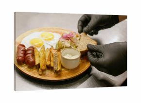Preparing food. Restaurant culinary. Chef hand in glove adding sliced bread to served hot dish. Appetizing dinner with potato egg sausage.