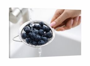 Woman washing blueberries in sieve at sink, closeup