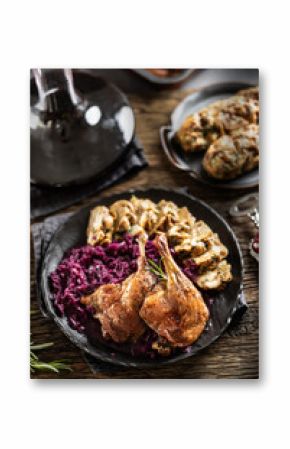 Portion of roast duck leg red cabbage homemade dumplings on plate and red wine on the background