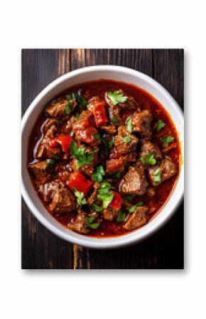 Hungarian goulash soup with beef, peppers, and herbs is served in a white bowl on a dark wooden table