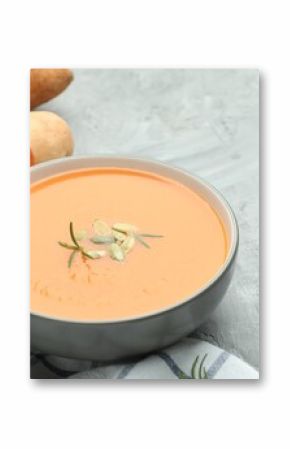 Delicious sweet potato soup with pumpkin seeds in bowl, vegetables and rosemary on grey textured table, closeup. Space for text