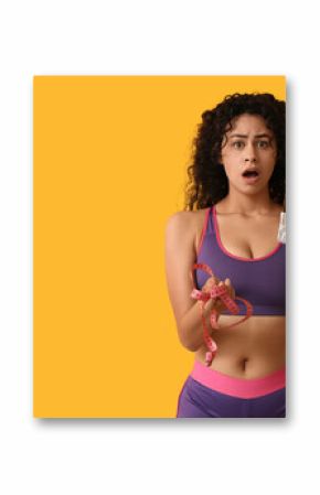 Shocked young African-American woman with sweet chocolate bar and measuring tape on yellow background