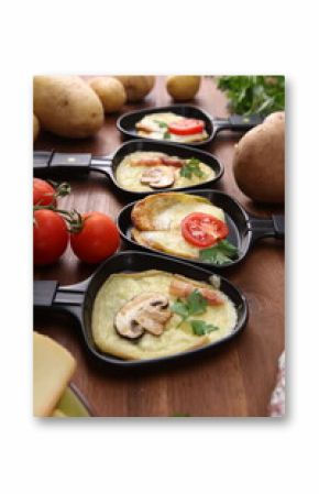 Delicious traditional Swiss melted raclette cheese served in individual skillets with salami and bacon