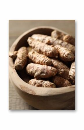 Raw turmeric roots in bowl on wooden table, closeup