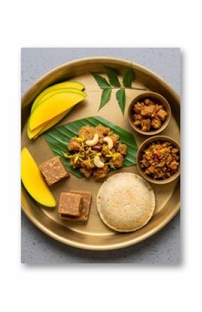 Traditional Indian thali with idli, banana, sweets, and curries on brass plate. Festive South Indian meal for Pongal, Onam, Vishu. Vegetarian cuisine concept.