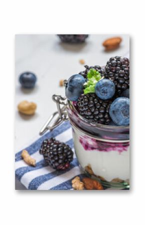 Yogurt parfait with blackberry, blueberry, granola, nuts and berry sauce in glass jar with fresh mint on white background. Layered Greek yoghurt with fresh berries. Healthy breakfast