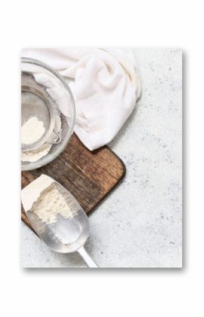 Bowl with flour, metal sieve, scoop and wooden board on light background