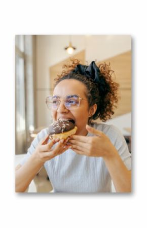 Portrait of a hungry young woman sitting in fast food restaurant and eating delicious doughnut.