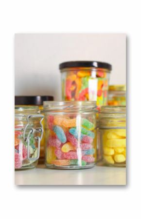 Tasty gummy candies in glass jars on light table, closeup