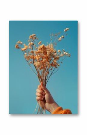 A hand holding a bouquet of dried flowers, against a bright blue sky. Captures the simplicity and natural beauty of dry floral arrangements.