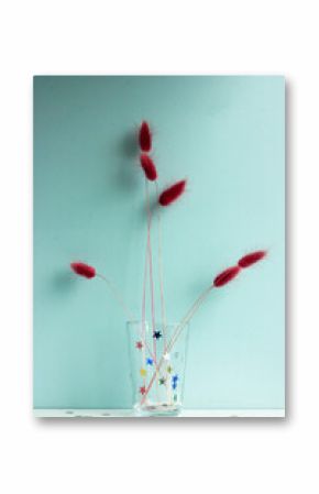 Purple dry flowers in a glass vase against a blue wall background 