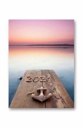 wooden pier with anchor and a 2026 from stones in sunset