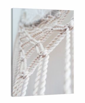 Close-up of a handmade macrame wall hanging. The intricate knots and patterns are visible, showcasing the craftsmanship and texture of the natural fibers. 