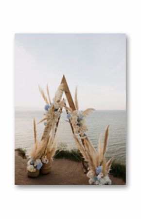 A beautifully crafted wooden arch, adorned with pampas grass and vibrant flowers, is perched majestically on a cliff, offering stunning views of the ocean