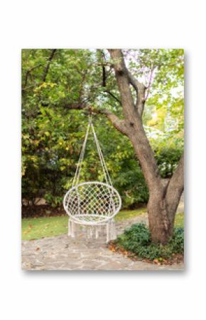 Comfortable hanging wicker white chair in summer garden. Cozy hygge place for weekend relax in garden. Hammock chair in boho style hanging on tree. Cozy exterior backyard. Concept of rest outdoor.  