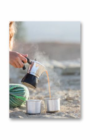 Woman pouring coffee boiled outdoor on the beach in two cups