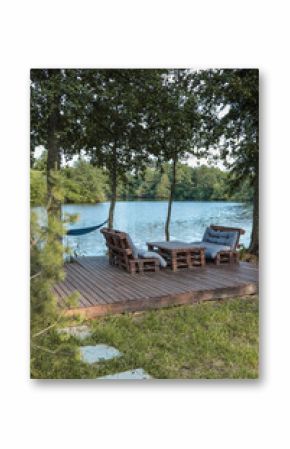 Wooden deck with handmade pallet furniture and soft cushions by a calm lake, surrounded by trees. A hammock and tree swing complete this peaceful outdoor retreat in nature