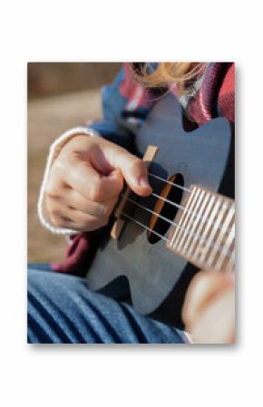 Close up of female hands playing guitar ukulele and singing relaxing enjoying outdoors on sunny autumn day. Hippie woman in boho style training playing musical instrument. Fall leaves autumnal weather