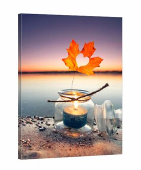 burning candle in a glass with colorful autumn leaves on the beach in fall season