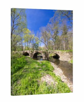 Old stone bridge crossing Doubrava river near Zasmuky in Czechia surrounded by spring greenery