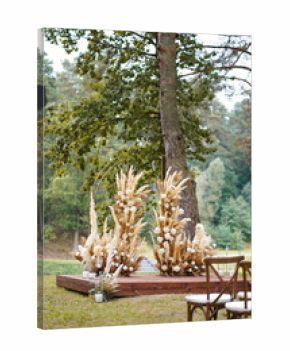 Same wedding arch with dried plants and white flowers, viewed from another angle among trees.