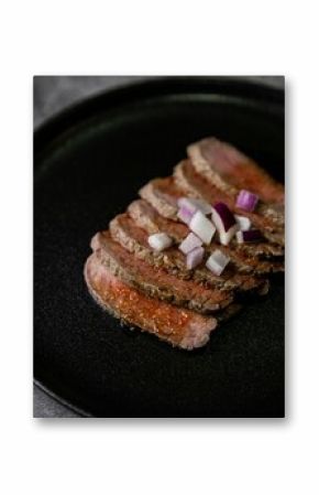 Closeup shot of steak tataki in sauce and onions on black plate with grey blurred background