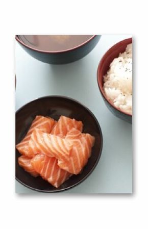 Overhead closeup of salmon chunks, steamed rice and soy sauce in dark bowls on a table