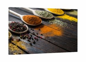 different spices in wooden spoons on a black wooden background