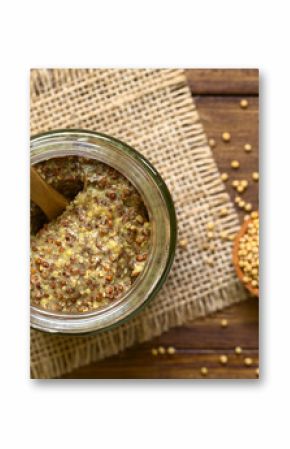 Whole grain mustard in glass jar, photographed overhead on wood natural light (Selective Focus, Focus on the top of the mustard)