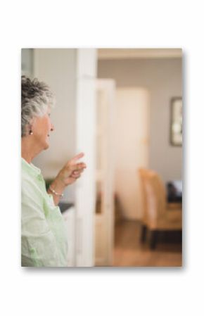Senior woman pointing toward dining space in kitchen, showing olive oil, checkered tablecloth