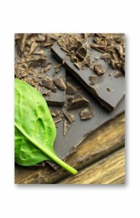Flat design showing spinach leaf lying diagonally on dark chocolate and pieces, shavings on wood