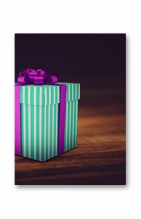 Flat design mint green striped gift box is sitting on wooden tabletop, with purple ribbon bow