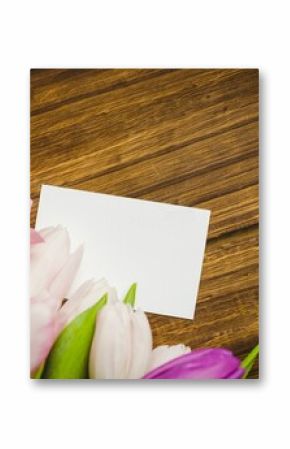 blank white rectangular card is lying atop wooden tabletop in flat-lay, with colorful tulip bouquet