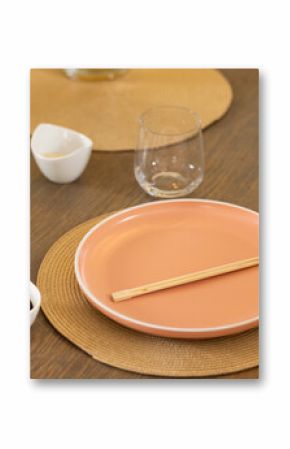 Chopsticks on pink plate with soy sauce and glass on dining table