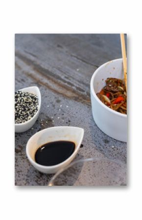 Chopsticks picking up noodles with sesame seeds and soy sauce on table, at home