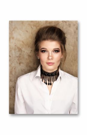 Beauty portrait. Beautiful young woman in white shirt against a metal wall. Stylish image, professional makeup, hair collected