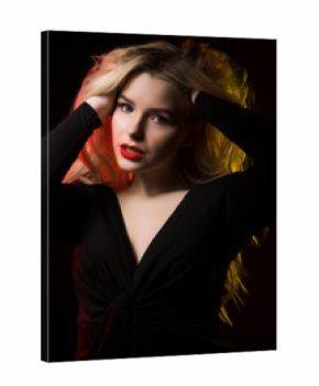 Glamorous young lady with bright makeup and long wavy hair posing over a black background