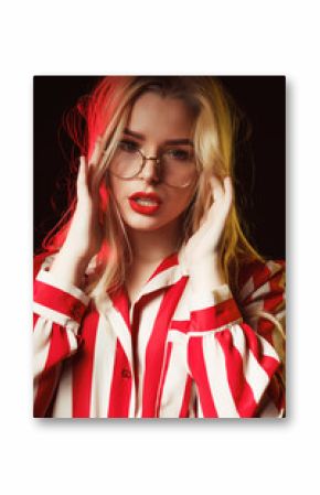Fashionable blonde girl in glasses wearing striped blouse, posing with red and yellow light
