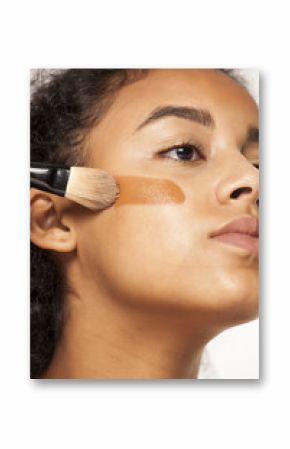 portrait of a young dark-skinned woman applying liquid makeup base with brush on her face on a white background