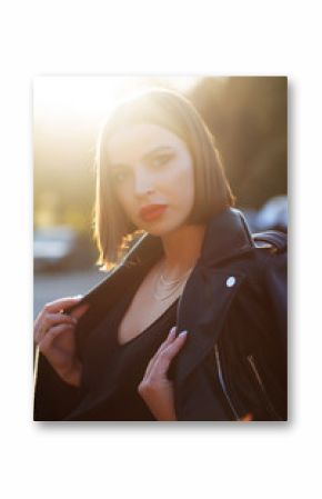 Street portrait of gorgeous brunette model wearing leather jacket, posing in soft evening sunlight