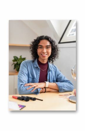 Asian makeup artist smiling while sitting at light wood attic desk surrounded by brushes and mirror