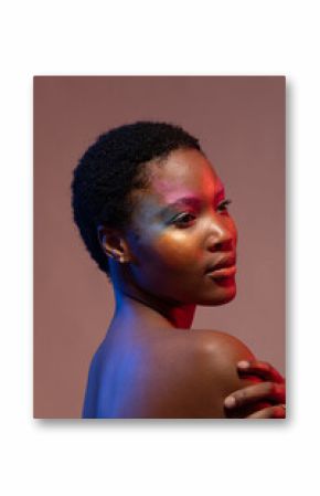 African american woman with short hair and colourful make up, looking away and holding shoulder