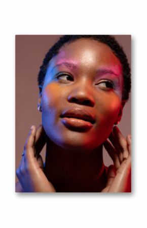 African american woman with short hair and colourful make up, looking away and touching neck